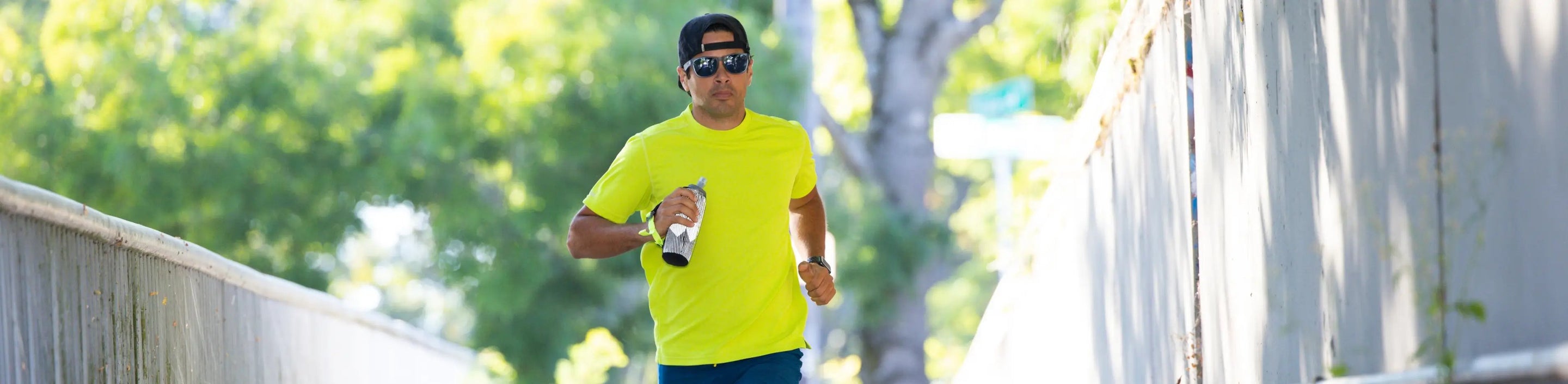 male runner wearing Nathan Sports Short Sleeve Shirt in bright yellow holding a handheld water bottle