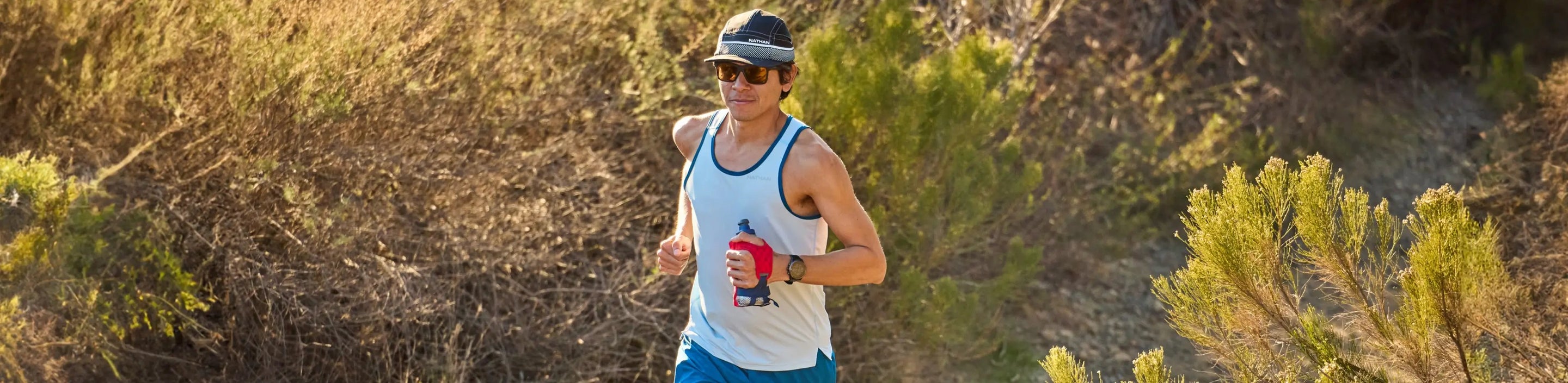 man running in Nathan Sports white tank top and holding handheld bottle