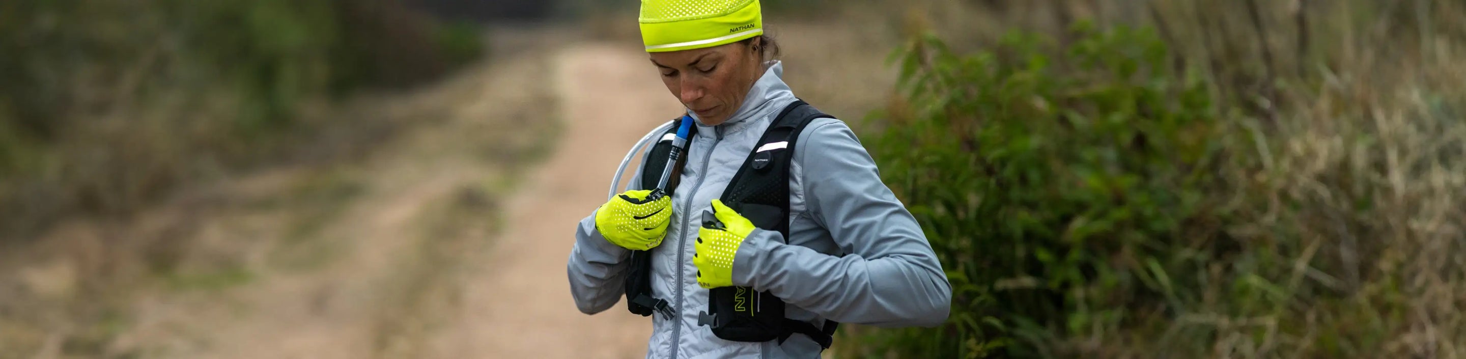 athlete stopped to side of trail in Nathan Sports HyperNight Reflective Beanie, Gloves, and a black hydration pack