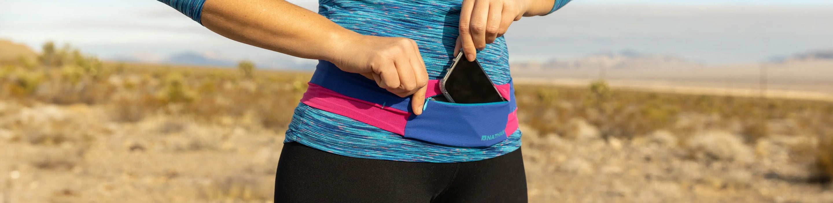 athlete wearing Nathan Sports Zipster Lite running belt putting phone into the zip pouch