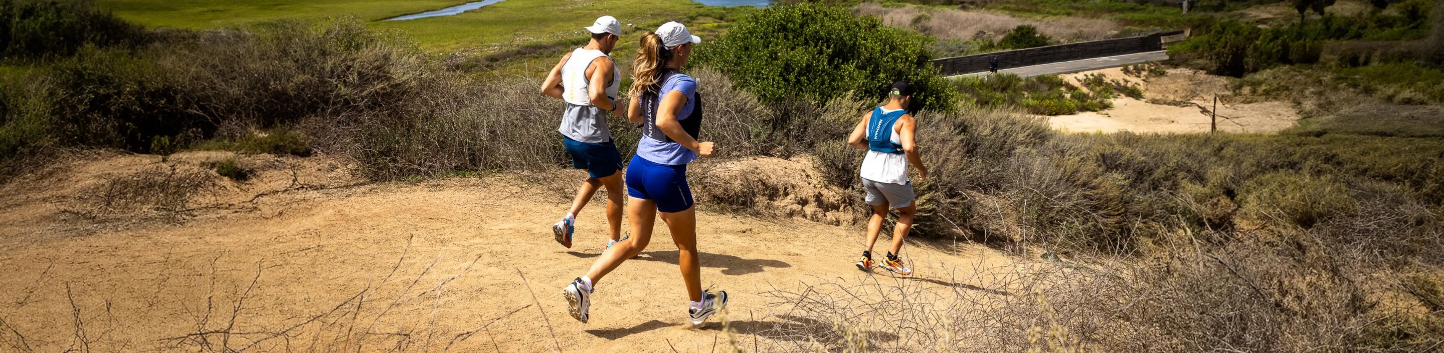 three trail runners wearing Nathan Sports apparel and hydration packs running down a dirt hill