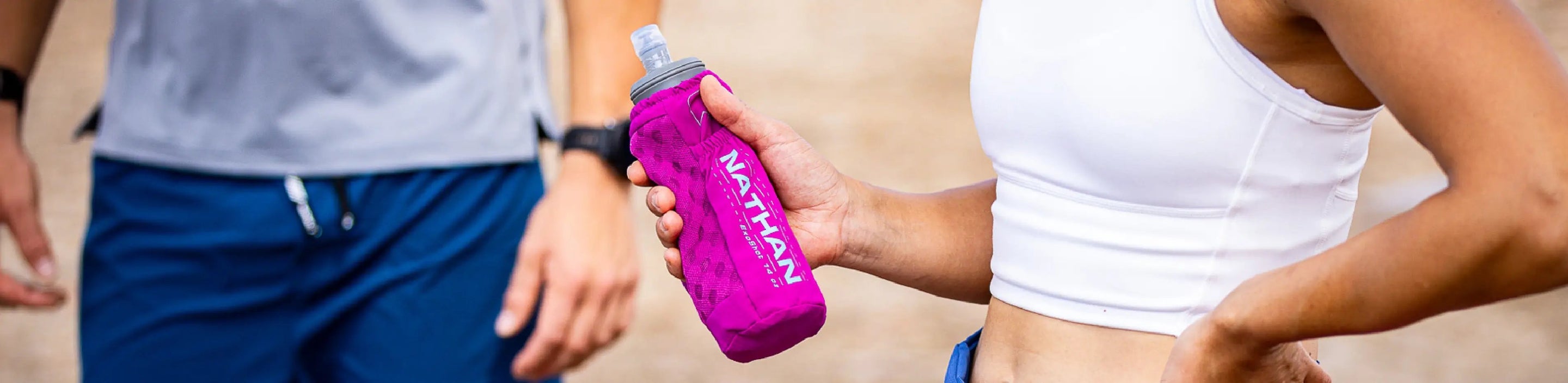 two athletes standing and one holding a Nathan Sports Handheld Bottle