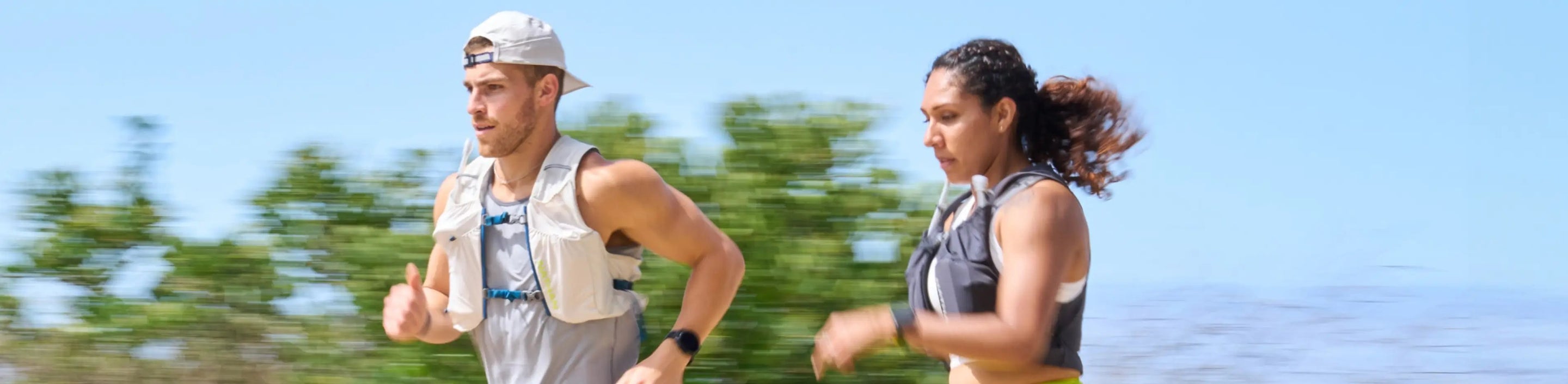 male runner in Nathan Sports backwards Run Cool Stash Hat and Hydration Vest, female running wearing hydration vest in black