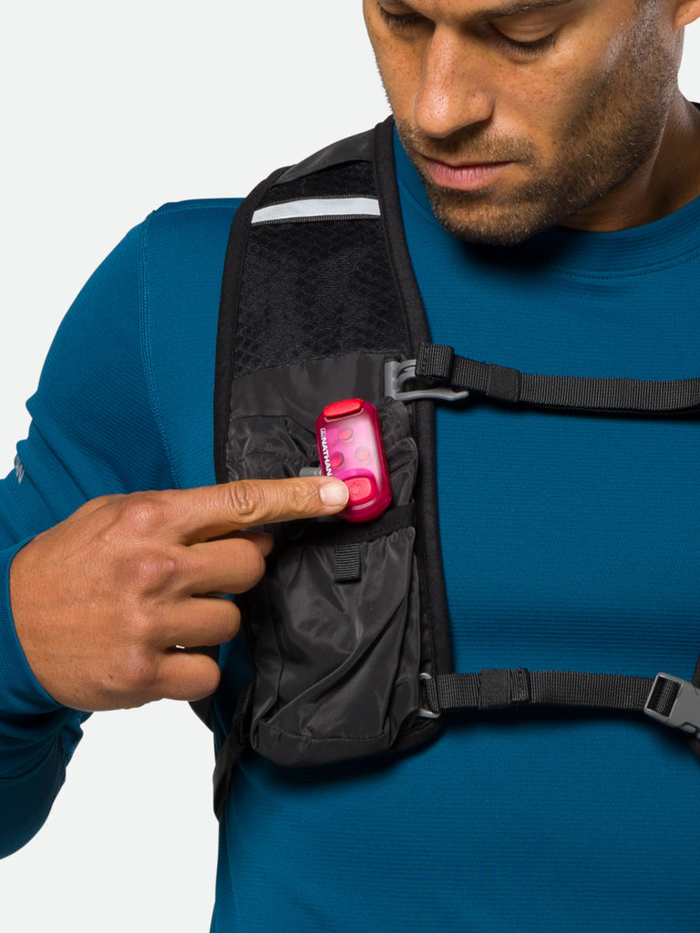 Nathan Strobe Light LED Safety Light Clip - Magenta - On Model - Turning on Clip Light Attached to Hydration Vest 