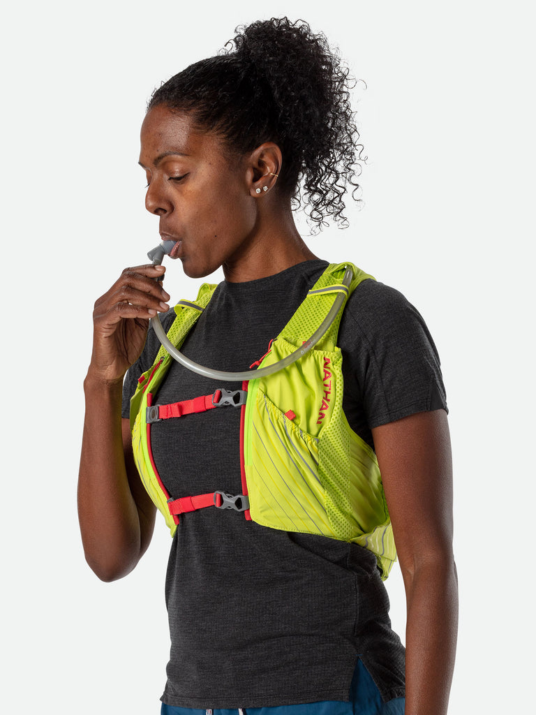Nathan Pinnacle 12 Liter Women's Hydration Race Vest - Finish Lime/Hibiscus Red - Female Runner Sipping from High Flow Bite Valve