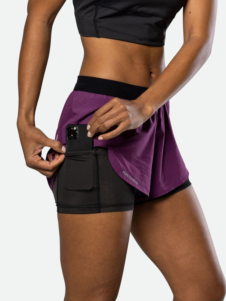 Nathan Women’s Front Runner Shorts 2.0 - Plum Purple - On Model - Pulling Cellphone from Front Liner Pocket